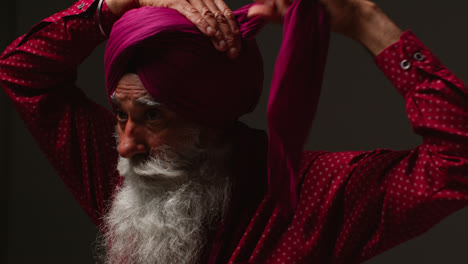 Primer-Plano,-Toma-De-Estudio-Con-Iluminación-Tenue-De-Un-Hombre-Sikh-Mayor-Con-Barba-Atando-Una-Tela-Para-Un-Turbante-Contra-Un-Fondo-Oscuro-4